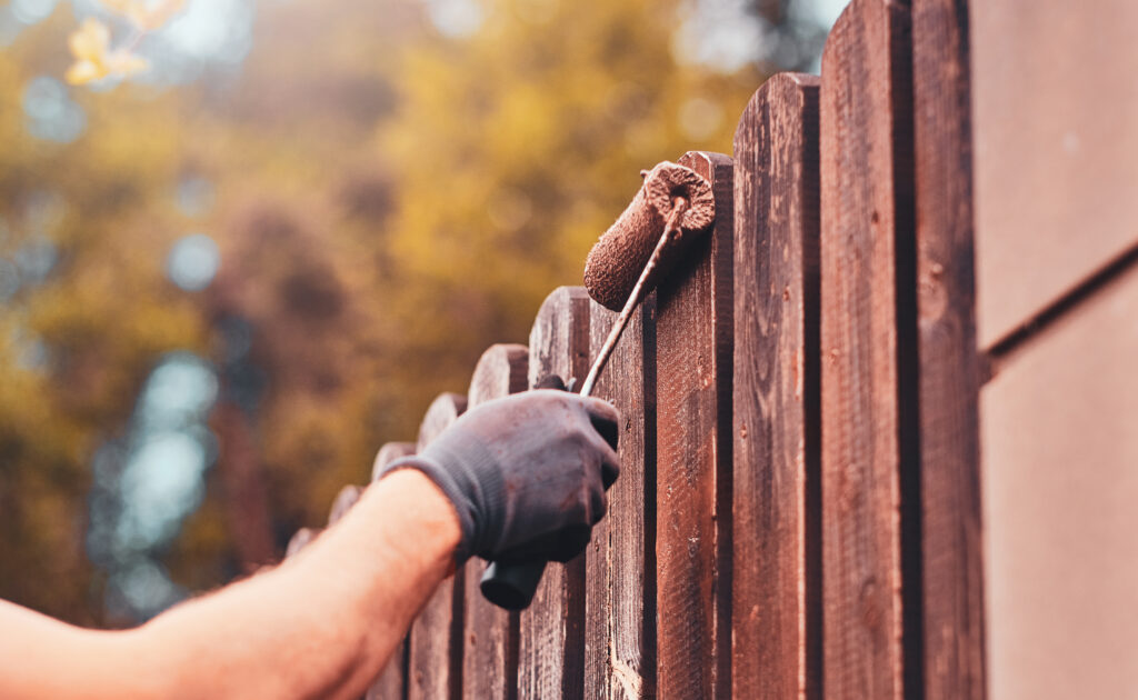 Une personne peignant une clôture en bois.
