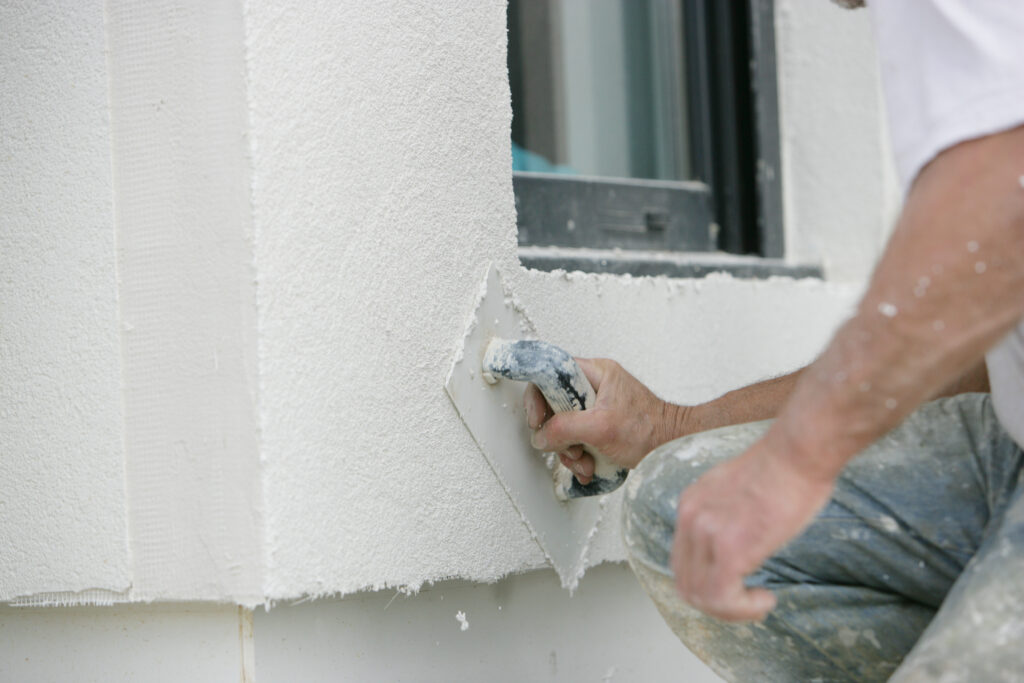 Une personne appliquant de l'enduit sur un mur extérieur.